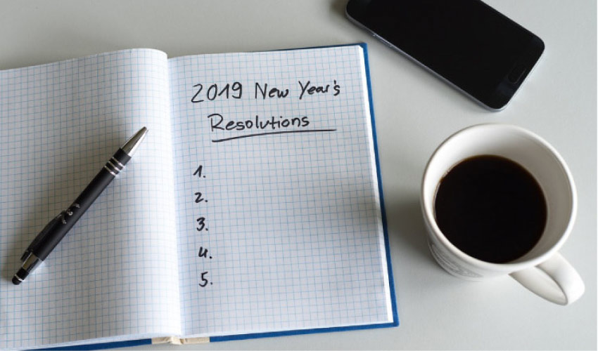 2019 new year's resolutions notebook, a pen, cup of coffee and a cell phone