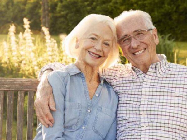 senior couple sitting on a bench smiling after learning about the longevity of their dental implants